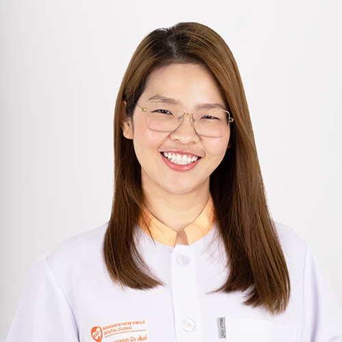 Portrait of a Thai female dentist wearing a white coat and glasses smiling
